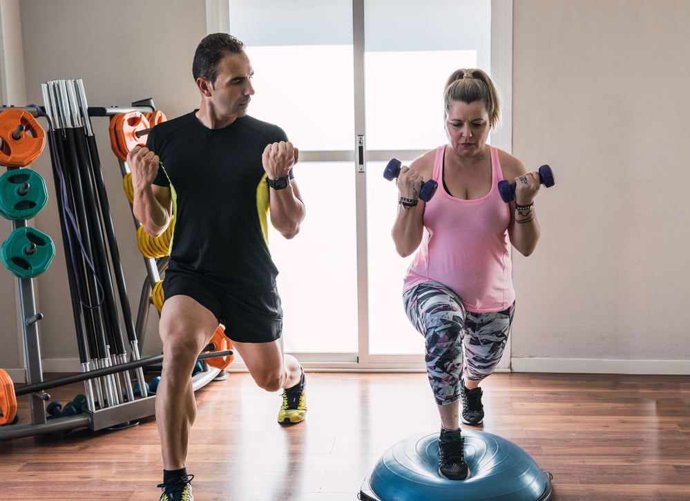 Personal trainer helping to do a weight exercise to a woman indoors