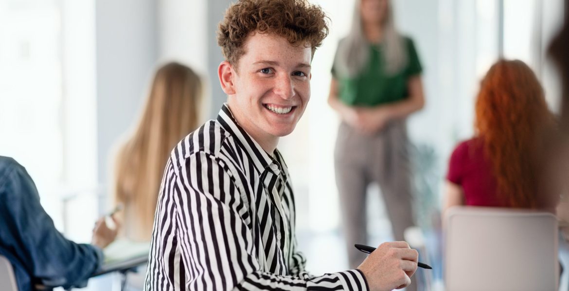 Portrait of young university student sitting in classroom indoors, looking at camera.