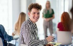 Portrait of young university student sitting in classroom indoors, looking at camera.