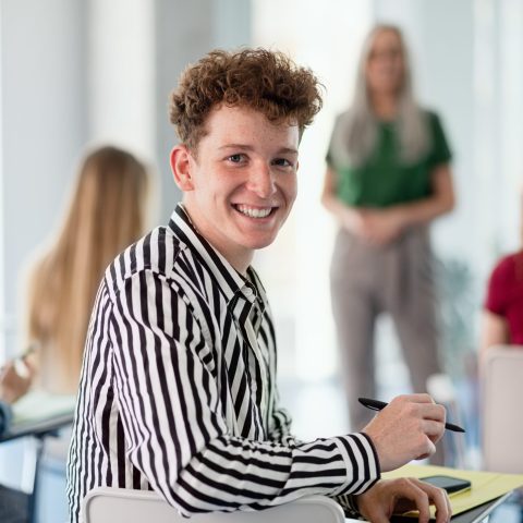 Portrait of young university student sitting in classroom indoors, looking at camera.