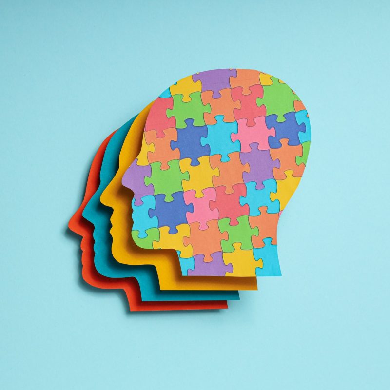 Paper human heads with colorful puzzle pieces on a light backgro