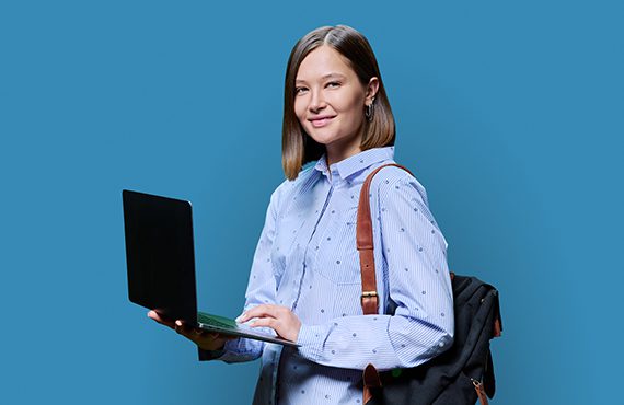 Young woman with laptop backpack on blue studio background. Smiling female student using computer, posing looking at camera. Technologies for education study, work, business, leisure, young people